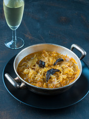 Cabbage soup in silver bowl and glass of white wine on dark background. Typical Christmas meal. Copy space,