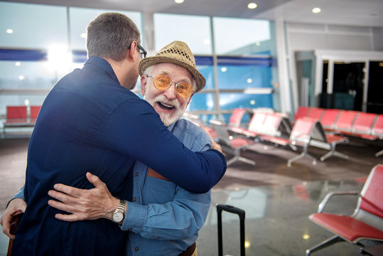 Happy moment. Portrait of pleased aged father in glasses and his grownup child are hugging each other while standing at airport lounge. Old man is looking at camera with glad. Copy space in right side