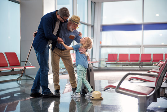Family embrace. Full length of positive mature father with gray-haired grandfather and little girl are standing at airport lounge and hugging. They are expressing happiness. Copy space in right side