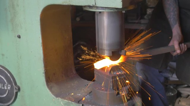 Blacksmith using machine to crush metal into place, sparks flying