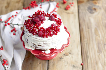 white cake with red berries and a branch on a wooden table