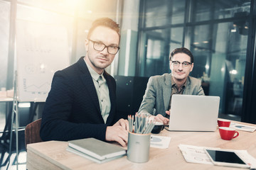 Portrait of smiling unshaven male working with serene affiliate while locating at table in office. Occupation and conversation concept