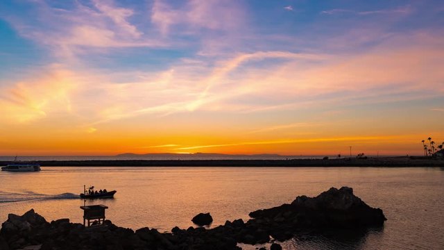 Sunset time lapse from California coast overlooking a harbor and island with blue and orange skies and boats passing