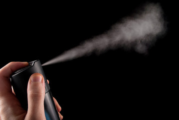 Deodorant spray in hand and white aerosol isolated on black background, close up