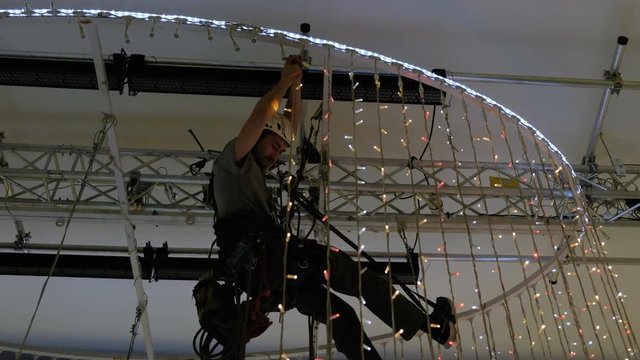 Industrial climber mounts Christmas decorations in the unsupported space in the shopping center