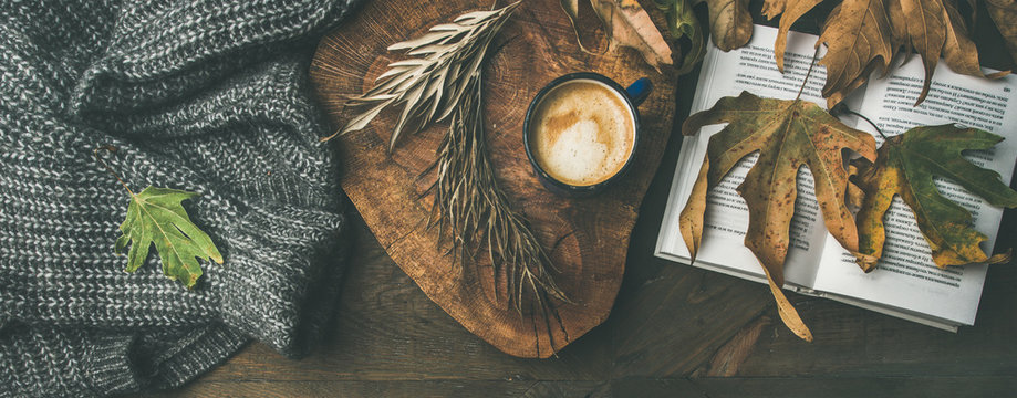 Autumn morning coffee concept. Flat-lay of knitted woolen jamper, wooden tray, mug of coffee, yellow fallen leaves and book over dark rustic wooden table background, top view