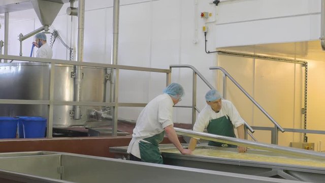 Employees in factory work on draining the left over liquid from a cheese vat