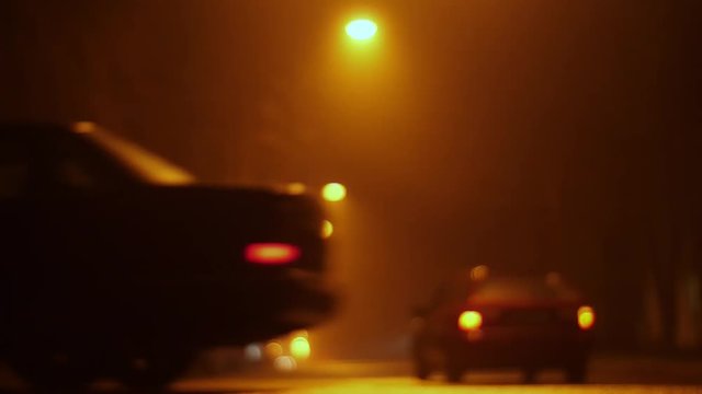 empty night street in the defocus and fog. lanterns hang over the road, cars drive through and people pedestrians cross the road