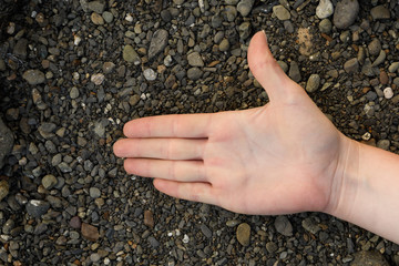 Woman open palm offering something lies on black pebbles