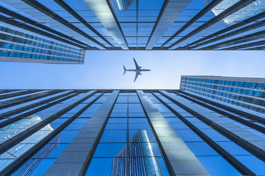 Tall City Buildings And A Plane Flying Overhead.