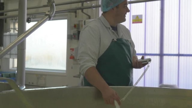 Employee checks the temperature of the milk inside cheese making factory
