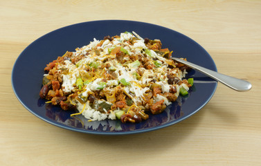 Chili on rice with sour cream and shredded cheddar cheese topping on blue plate with fork