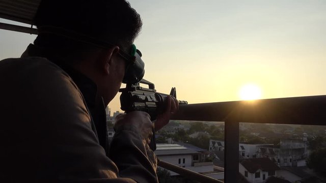 Man silhouette holding machine gun at sunset sky