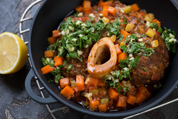 Osso buco made of cross cut veal shank with gremolata in a cast-iron pan, close-up, selective focus