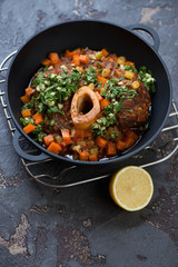 Cast-iron pan with osso buco and gremolata over brown stone background, studio shot, selective focus