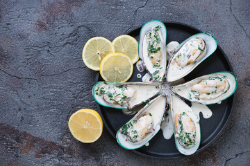 Kiwi mussels served with cheese sauce and lemon, top view with copyspace on a grey cracked asphalt background, horizontal shot