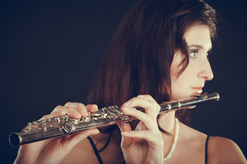 Woman playing transverse flute on black.