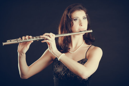 Woman playing transverse flute on black.