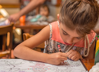 7 year old caucasian girl enjoys herself colouring the menu for children while on vacation in San Diego, California.