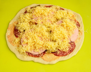 raw pizza with cheese and mushrooms on a green background