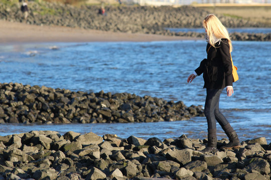 schlanke Frau mit blonden Haaren klettert &uuml;ber einen Steinwall am Elbufer.Where: Blankenese, Hamburg .When: 23.10.2011.
