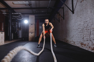 Front view of Young woman working out with battle ropes in cross fit gym