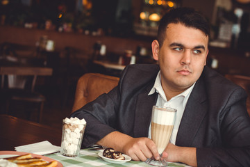 Confident young plus size businessman in suit enjoying a cup of coffee while having work break lunch in restaurant, young intelligent man or entrepreneur relaxing in outdoors cafe looking pensive 