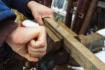 A man with strong hands clamps in a metal vice a wooden block