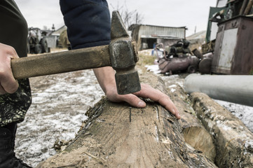 The village man hammers a nail into a wooden log using an old hammer
