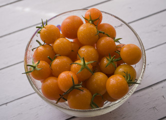 Organic yellow cherry tomatoes in glass bowl on white wooden table.