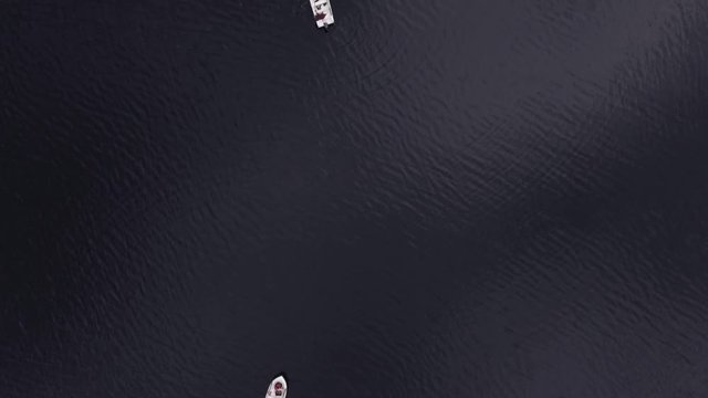 Shooting from helicopter flying over a pond, sea, ocean. Fishermen are sitting in fishing boats in the middle of the sea in Norway, Europe. Smooth surface of the sea with a ripple on the water
