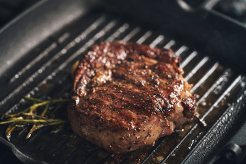 cooking rib eye steak with herbs on grill pan