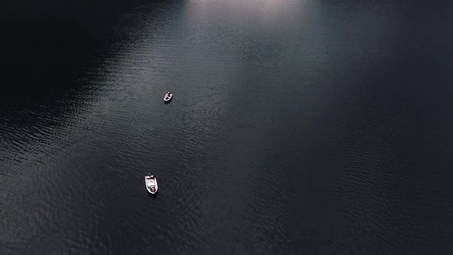 Shooting from helicopter flying over a pond, sea, ocean. Fishermen are sitting in fishing boats in the middle of the sea in Norway, Europe. Smooth surface of the sea with a ripple on the water