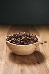 roasted coffee beans in wood bowl on table with dark background