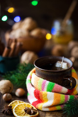 Winter cold and influenza concept. Cup of herbal tea wrapped in warm knitted scarf with colourful stripes and honey, cinnamon sticks and nuts at the background