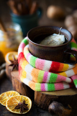 Winter cold and flu concept - Cup of herbal tea wrapped in warm scarf with a jar of honey and cinnamon at the background