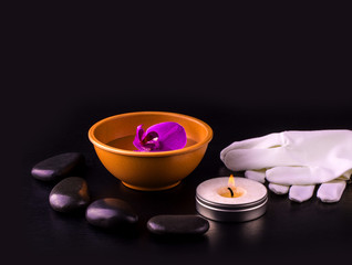 Beautiful spa composition with pink orchid on cup, stones and white gloves on black wooden table.