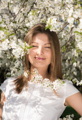 Vertical portrait of a young attractive woman in the flowered garden. Smile with your eyes closed