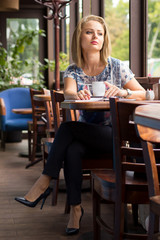 Young Business Woman in the Cafe with a Cup of Coffee and a Phone 
