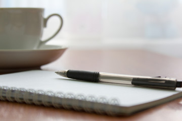 blank white notebook, pen and cup of coffee on the desk