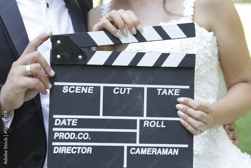 Wall mural Happy beautiful bride and groom, woman holds clapper board, cinema board 