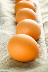 Raw brown chicken eggs in one row on burlap on a white wooden table. Ingredients for cooking.