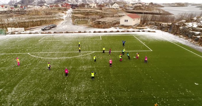 LOFOTEN, NORWAY – FEBRUARY,2017 : Aerial shot of football pitch on a cloudy day with kids playing and snowy mountains in view