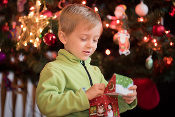 5 years old boy lies in front of the Christmas tree and looks at the  colorful lights and candle