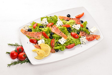 Salmon salad, feta cheese, salad leaves and fresh vegetables on the plate. On a wooden background. Top view. Free space for text.