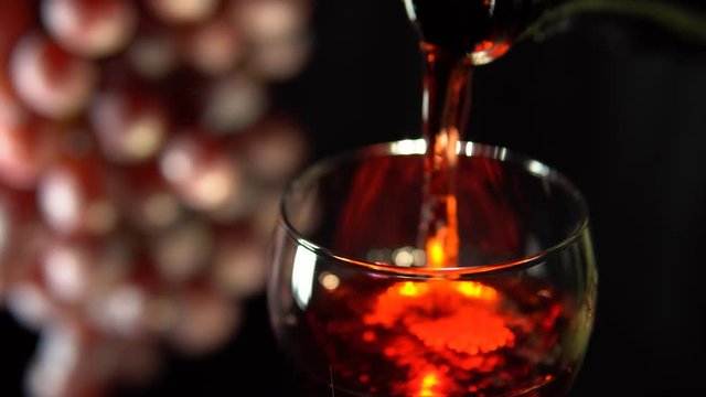 Red wine is poured into a glass next to rotating the grapes. A pink alcoholic drink pours from a bottle on a black background.