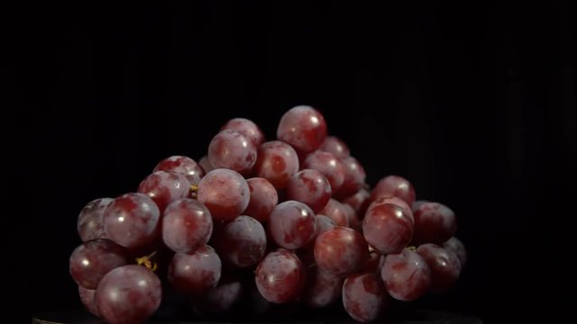 Bunch of juicy ripe purple grapes rotates against black background. Closeup view shot with seamless looping.