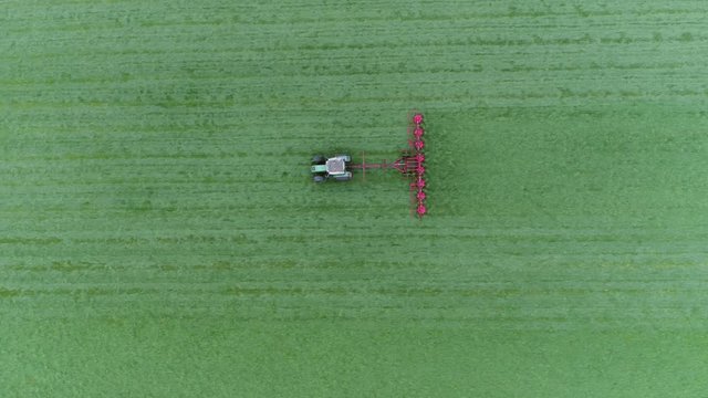 Aerial top-down view of green grass farm field with tractor raking grass so grass can dry faster and becomes dried grass or hay then be picked up and kept for cattle fodder for winter food 4k quality