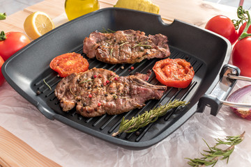 Grilled steak on grill pan with tomatoes on wooden background