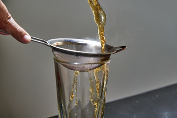 Pour hot tea into a glass through a sieve.